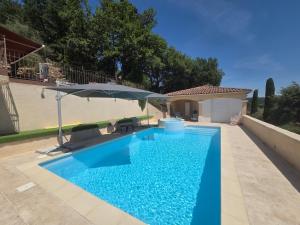 a blue swimming pool with an umbrella next to a house at Les Restanques de Camélie in Saint-Thomé