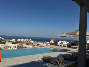 a swimming pool with chairs and umbrellas and the ocean at Ostria View Resort in Mikonos