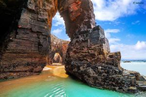 an arch in a rock formation in the water at Apartamento Playa Foz in Foz