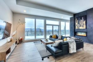 a living room with a black leather couch and large windows at Tremblant Summit: Travel Experience Beyond Compare in La Conception