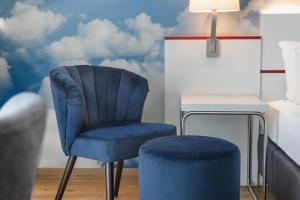 a blue chair and stool in a bedroom with clouds wallpaper at Hey Lou Hotel Friedrichshafen in Friedrichshafen +27 photos