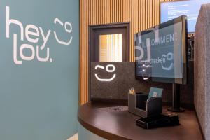 a desk with a tv and a computer on it at Hey Lou Hotel Hildesheim in Hildesheim