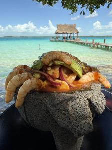 a person holding a sandwich with the ocean in the background at Mayan Playa Bacalar in Bacalar