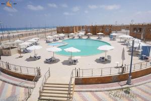 a large pool with umbrellas and tables and a beach at Ghazala resort in Marsa Matruh