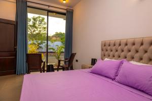 a bedroom with a purple bed and a large window at Port Royal Residence in Trincomalee