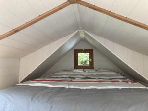 a bed in a white attic with a window at Tiny House Insolite avec Escape Game in Chanzeaux
