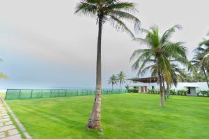 two palm trees in a field with a building at Shelter Beach Resort in Mahabalipuram