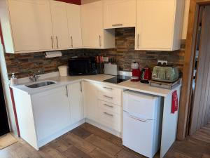 a kitchen with white cabinets and a sink and a refrigerator at Glan Llyn Farm House in Mold