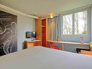a room with a bed and a desk and a tv at ibis Poitiers Beaulieu in Poitiers