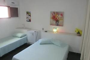 a white room with two beds and a refrigerator at Pousada Tia Lucia in Saquarema