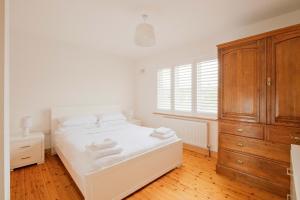 a white bedroom with a bed and a wooden cabinet at Beautiful 3 Bedroom House in Ennistymon