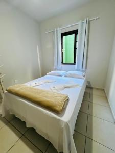a bed with white sheets and a window in a room at Casa do Carol Sana in Macaé