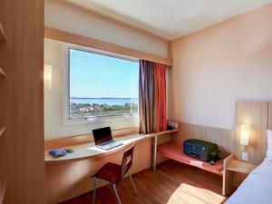 a hotel room with a desk with a laptop and a window at ibis Vitoria Praia do Canto in Vitória