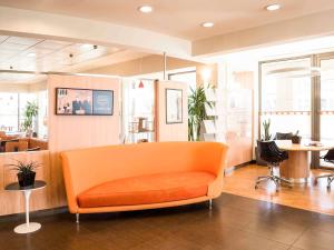 an orange couch in a room with tables and chairs at Ibis Como in Grandate