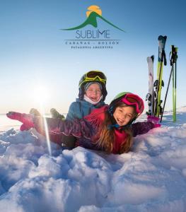 two girls laying in the snow in the snow with skis at Cabañas Sublime Bolson in El Bolsón