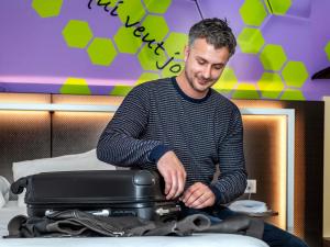 a man sitting on a bed with a suitcase at ibis Styles Strasbourg Stade de la Meinau in Strasbourg