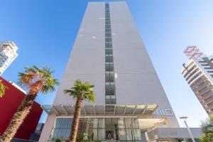 a tall building with palm trees in front of it at Lindo studio equipado em apartamento clube com academia e conforto no centro de Curitiba - MID Home in Curitiba