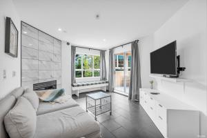 a white living room with a couch and a tv at Central Alpine Condo in Whistler