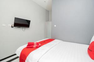 a bedroom with a white bed with a red blanket and a flat screen tv at RedDoorz Plus near Politeknik Negeri Malang in Malang