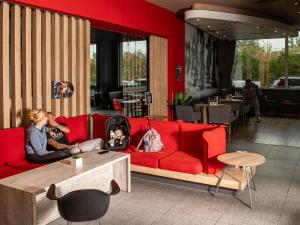 a woman and child sitting on a red couch in a restaurant at Ibis Sofia Airport Hotel in Sofia