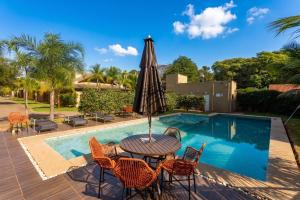a table with an umbrella next to a swimming pool at Casa Charme no Centro de Bonito - Condomínio Eco Bonito in Bonito