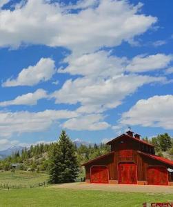a red barn in a field with a cloudy sky at Couples Country Getaway in Pagosa Springs +1 photo