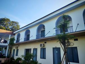 a white building with arched windows and a tree at Một Eco-Lodge in Tân Phú