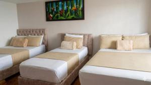 three beds in a room with a painting on the wall at Hotel Iam Armenia Quindio in Armenia