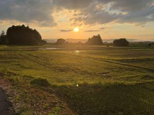 a field with the sun setting in the distance at Hotel The Namie Terrace in Namie