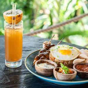 a plate of food with an egg and meat and a drink at Kima Surf Camp Bali Seminyak in Seminyak