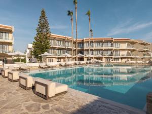 a resort pool with lounge chairs and palm trees at Atlantica Thalassa Hotel in Kos