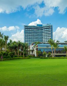 a large building with palm trees in front of a field at Renaissance Haikou Hotel in Haikou