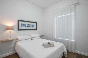 a white bedroom with a white bed and a window at Caracal 54 in Yzerfontein