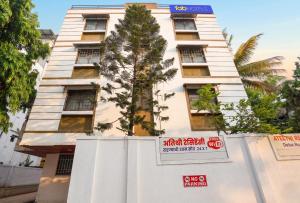 a tall white building with a tree in front of it at FabHotel Ateethi Residency in Pune