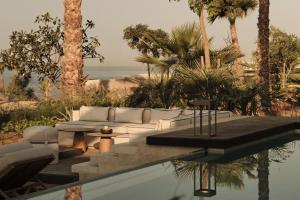 a pool with a couch and a table and palm trees at Rosewood AMAALA in Amala