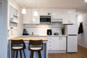 a kitchen with white cabinets and two bar stools at Sea Breeze Apartment in Mandurah