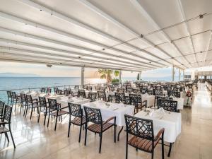 a restaurant with white tables and chairs and the ocean at Korumar Hotel Deluxe in Kuşadası