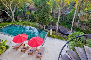 a swimming pool with two red umbrellas and chairs at Labak River Hotel by EPS in Ubud