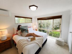 a woman sitting on a bed reading a book at Palacete Beach - Resort Style Stay in Culburra Beach