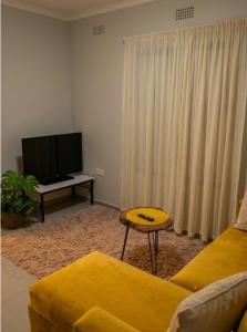 a living room with a yellow couch and a flat screen tv at Maun self-catering unit in Maun