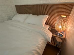 a bed with white sheets and a lamp on a table at The Greenery Omok in Seoul
