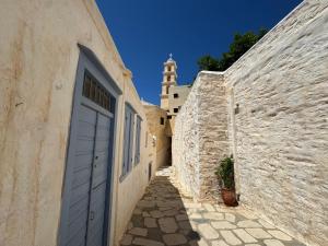an alley with a white door and a tower at Litharaki Guest House in Ano Syros