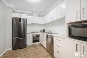 a kitchen with white cabinets and a stainless steel refrigerator at KozyGuru | Penrith | Spacious Ground Floor Gem in Penrith