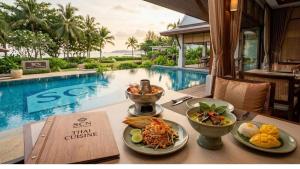 a table with food on it next to a swimming pool at Wellness Resort Rayong Managed by SCN in Ban Huai Pla Kang