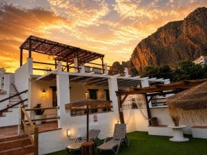 a building with chairs and a sunset in the background at El Charcon Alojamiento Rural in El Chorro