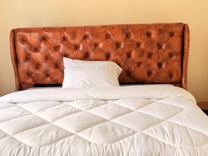 a bed with a leather headboard and white sheets at Volcanoes Stay Musanze in Kigali