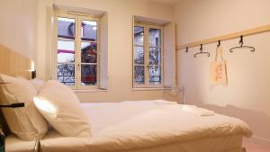 a white bed in a room with two windows at Mustard Hostel in Dijon