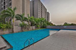 a large swimming pool with palm trees and buildings at Weekend Address By Farmville in Surat