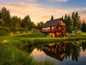 a barn sits next to a lake at sunset at Peaceful Nature Cottage near Talsi with Hot Tub, Sauna & Pond, Camping Ives in Talsi