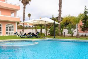 a couple sitting in chairs under an umbrella next to a swimming pool at Hotel Caldas Internacional in Caldas da Rainha